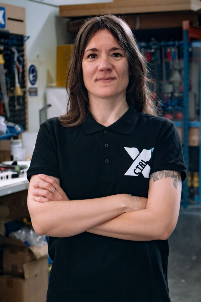 Patricia Huertas Villa, maquetista en CTRL X, posando con una camiseta negra frente a un taller de diseño.